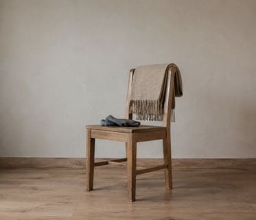 Una silla de madera con una manta doblada en el respaldo, en la sala